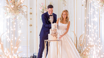 front-view-bride-groom-standing-bright-stage-with-decoration-cutting-wedding-cake-together 2
